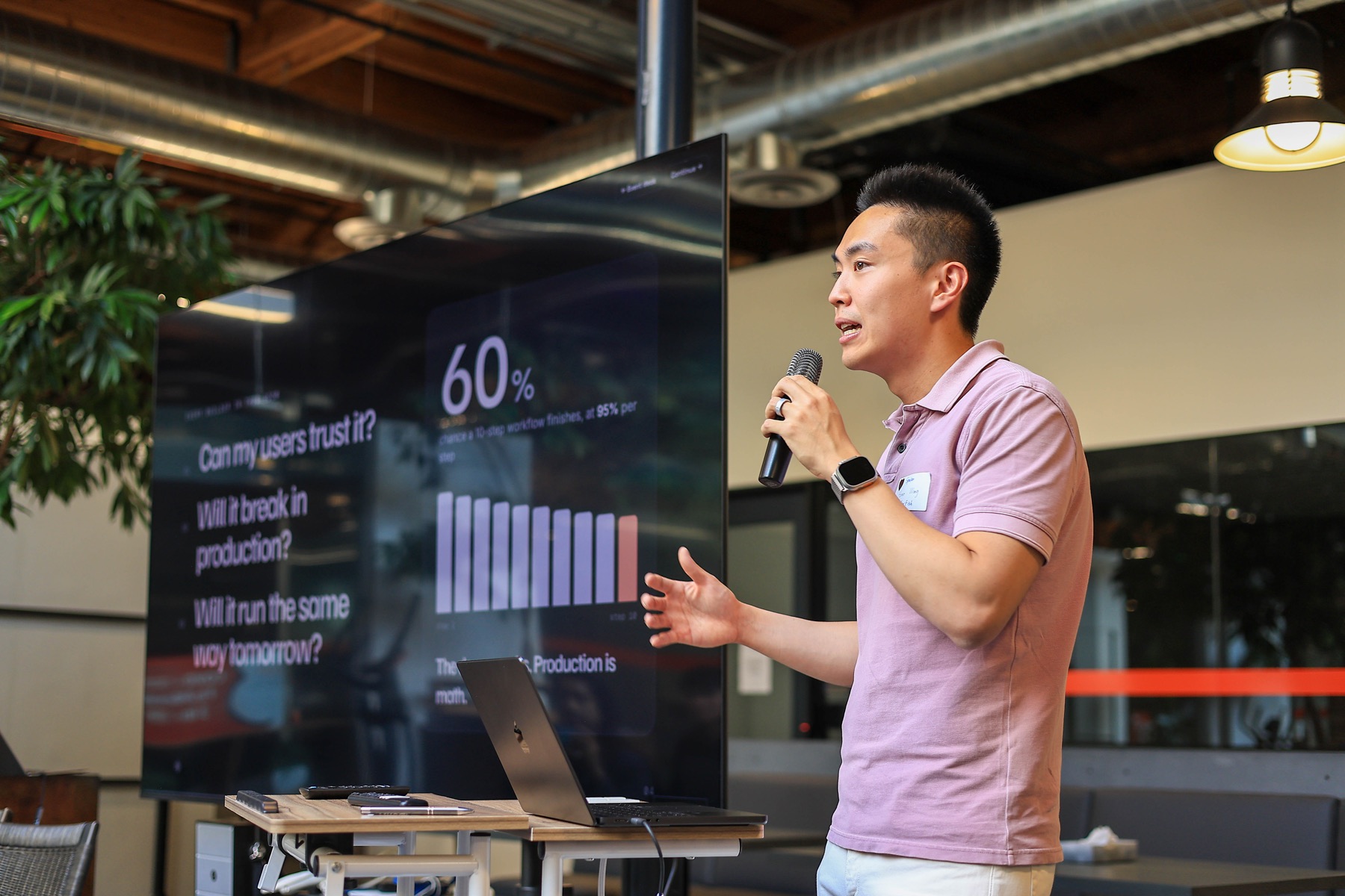 A speaker presenting questions about production reliability at AI Infra Signal