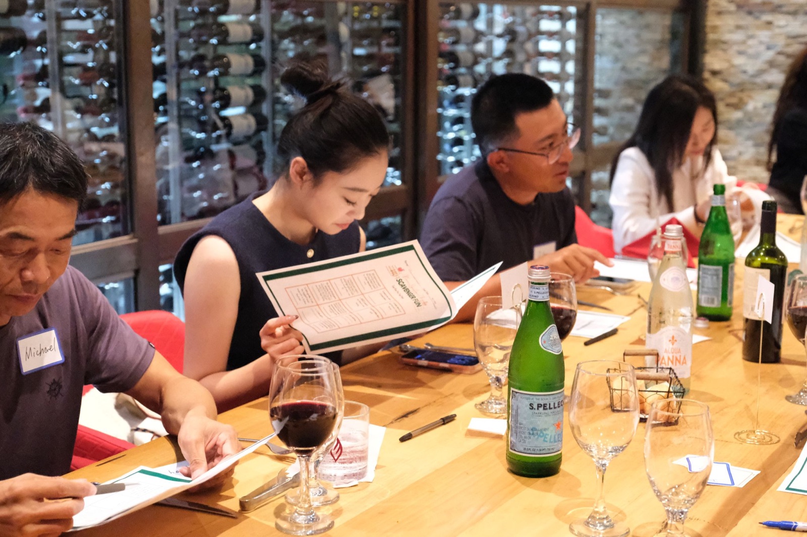 Founders reading the dinner menu and talking across a long table with wine service